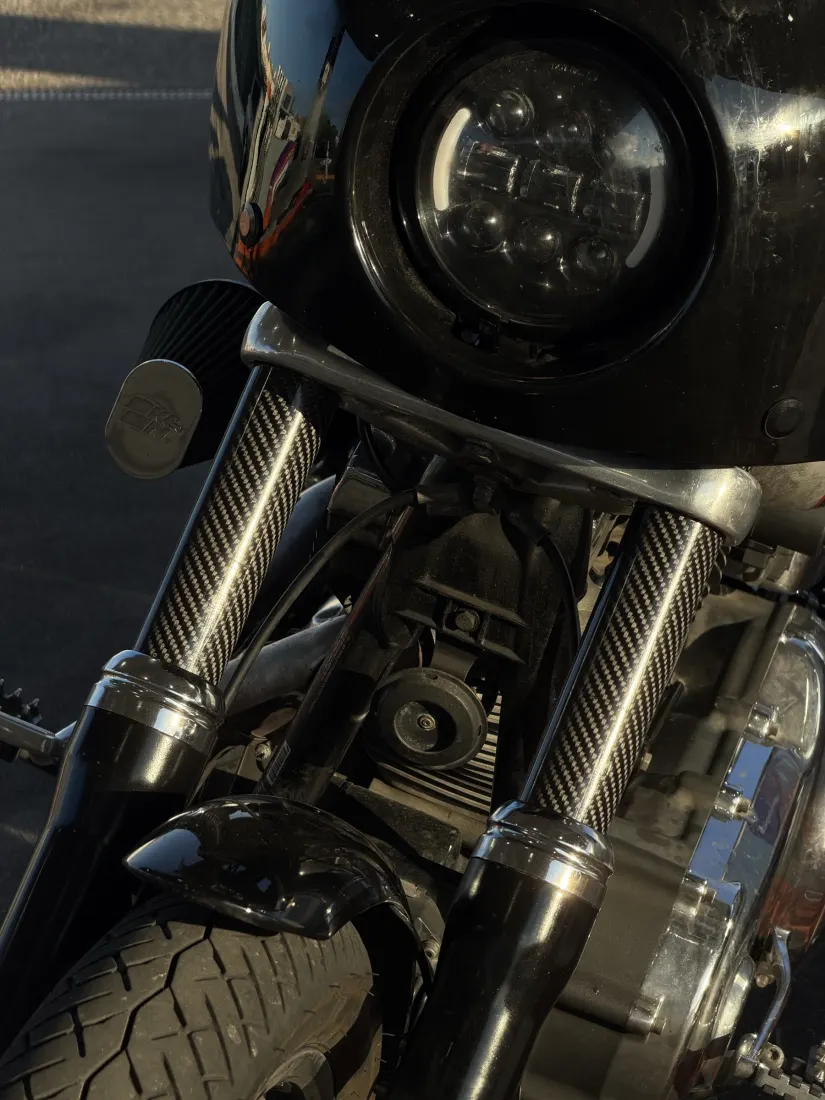 Close-up of a black motorcycle's headlight and forks, polished and catching the evening sun