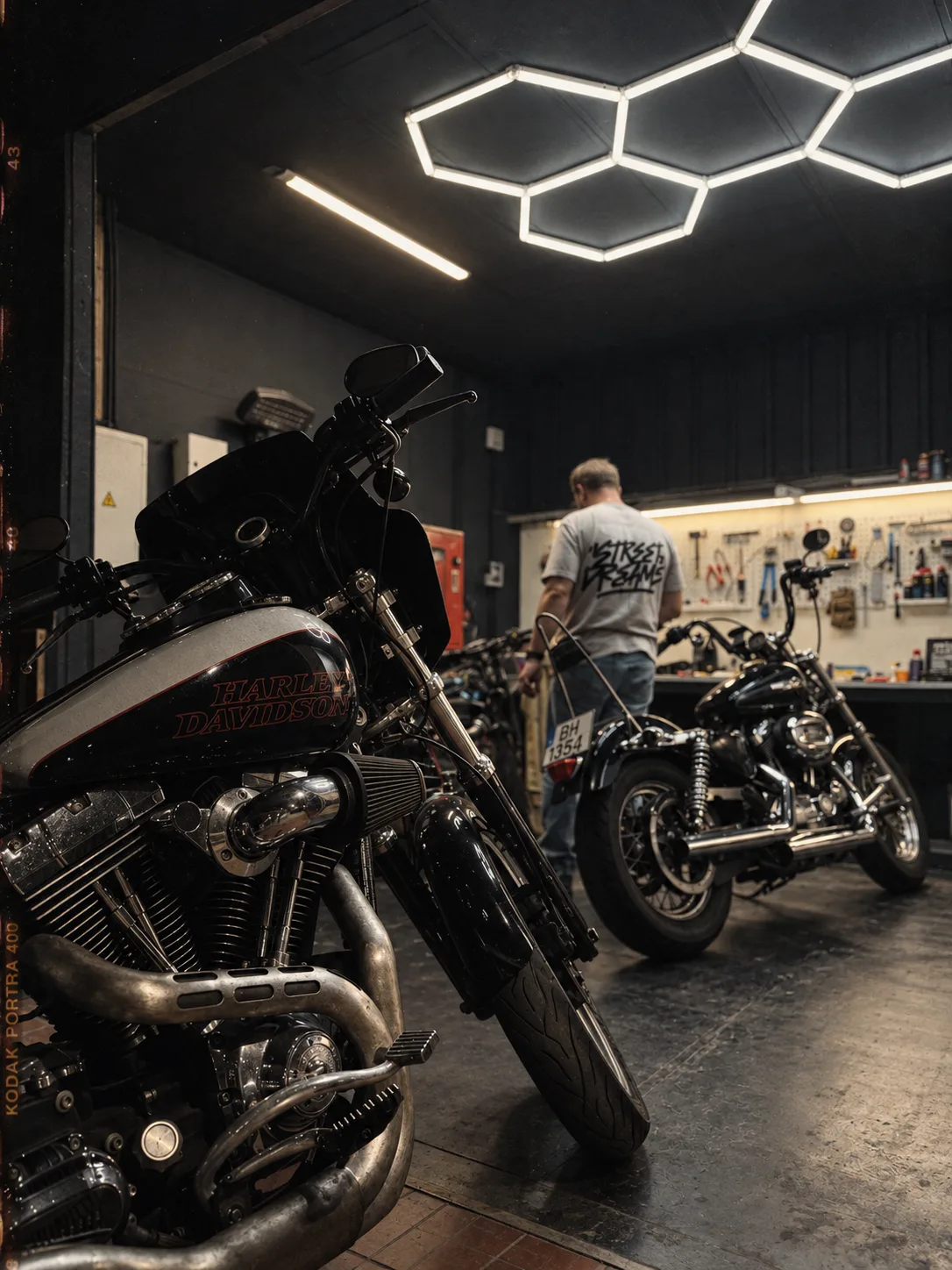 Two motorcycles in the garage, a mechanic working at the bench behind them under the hex light