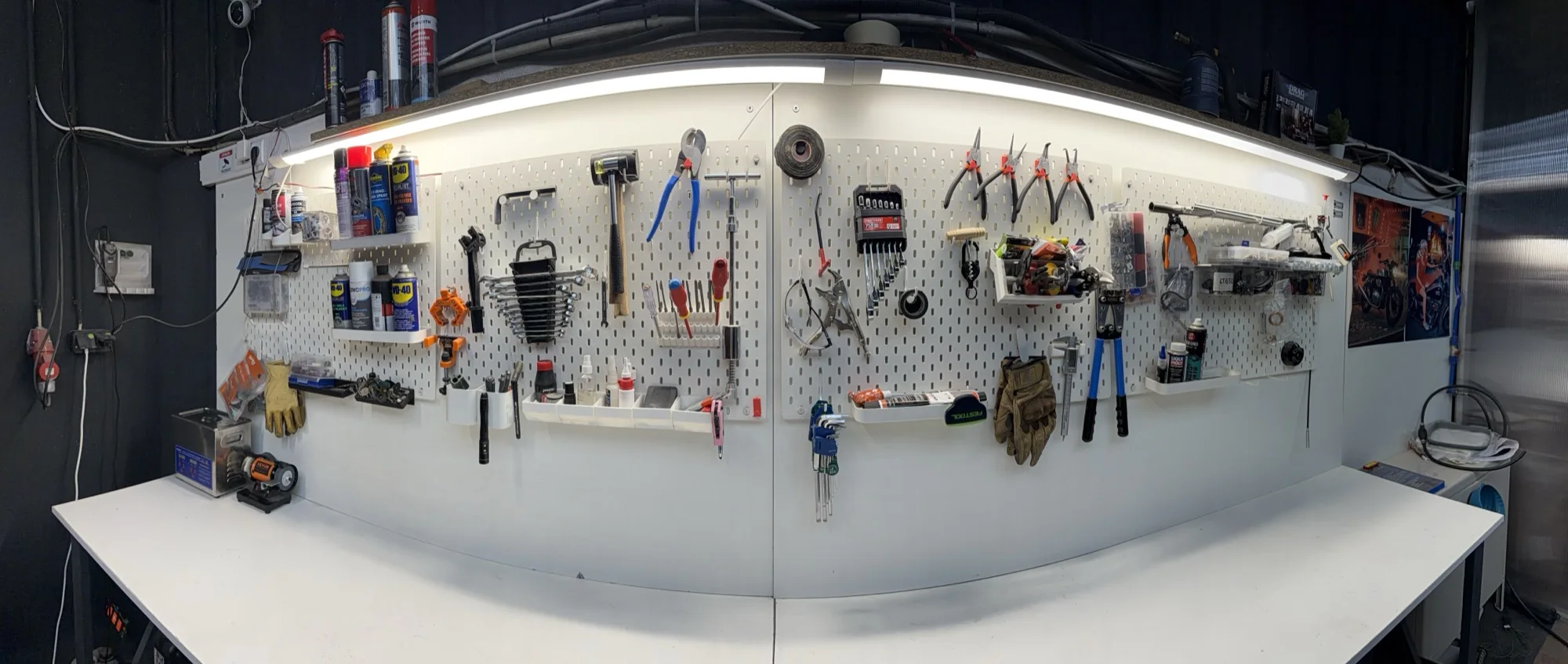 The workshop tool wall: spanners, pliers, screwdrivers and sprays on the pegboard above the bench