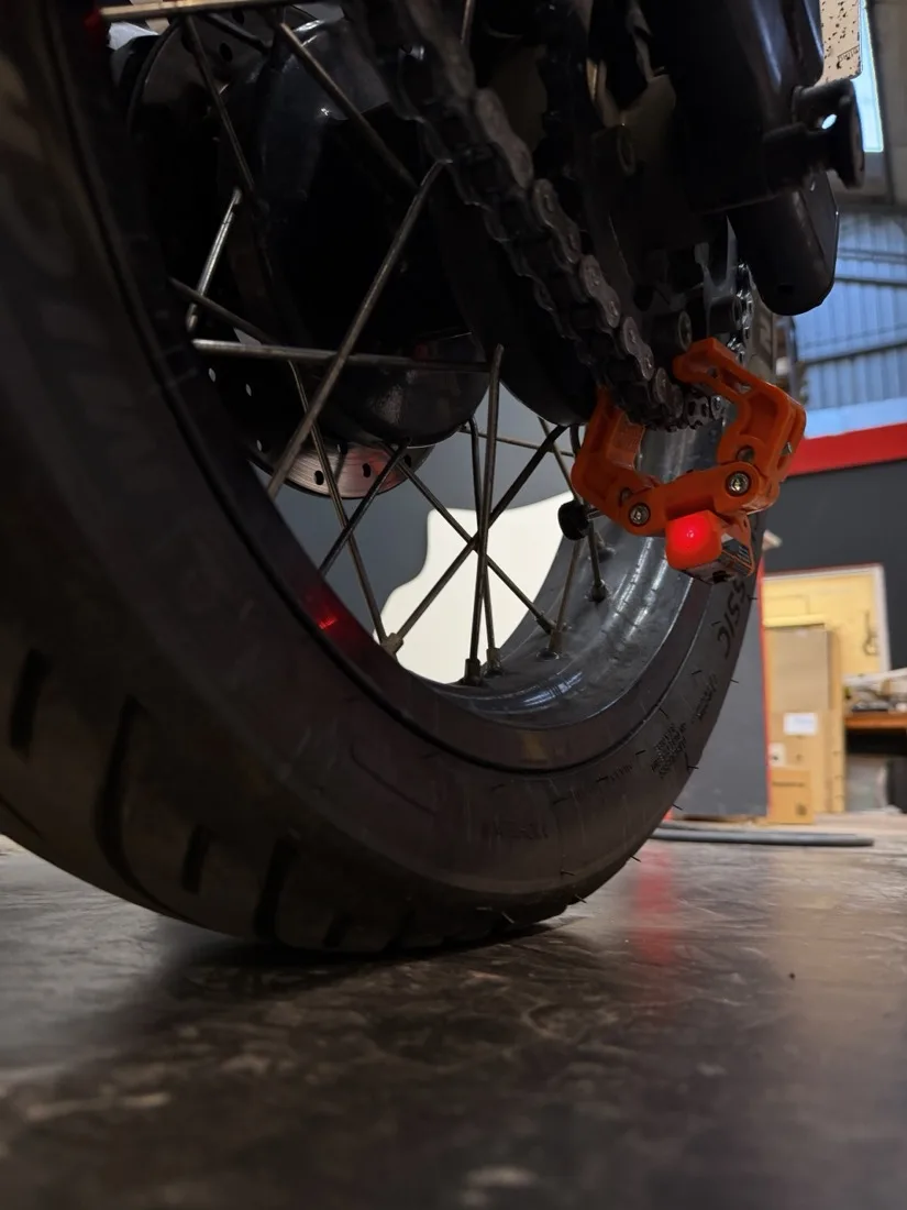 An orange laser tool clamped to the rear sprocket, its red line running along the chain