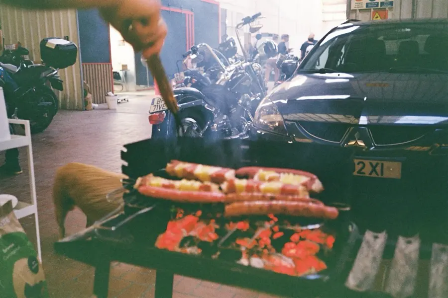 Sausages on the grill, a car and a row of bikes behind