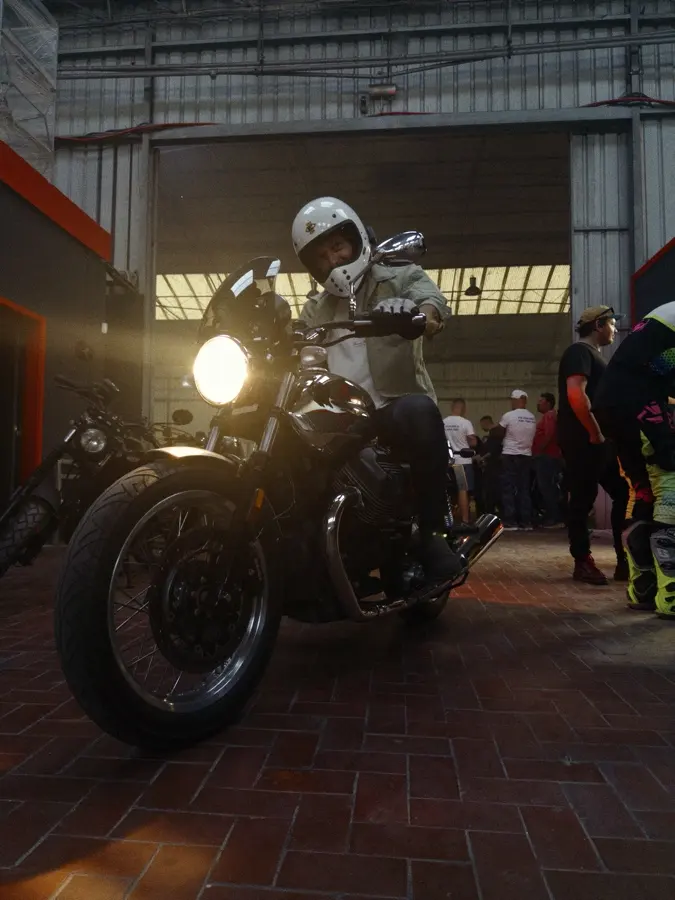 A rider in a white helmet rolling out through the crowd, headlight on